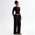 Woman wearing a black long-sleeve top and black wide-leg pants on a white background