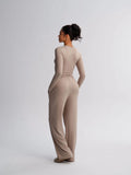 Woman wearing a beige long-sleeve jumpsuit on a light gray background