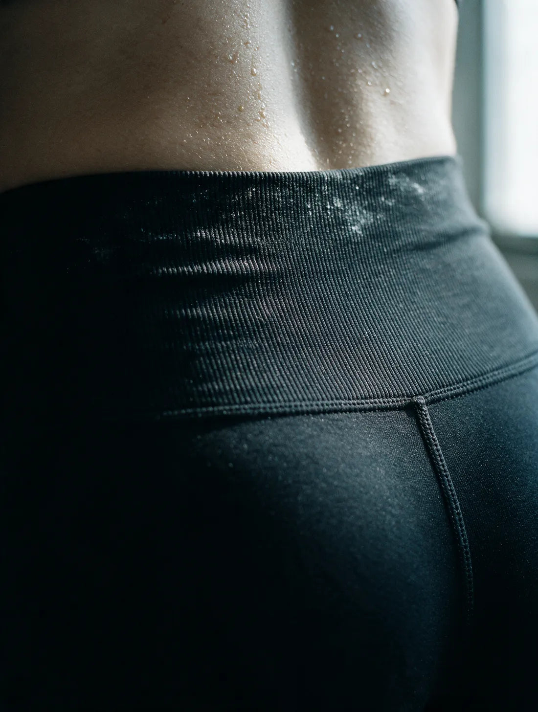 Close detail of the wide high-waist band lying completely flat against the skin of a lifter's lower back, chalk dust across it.